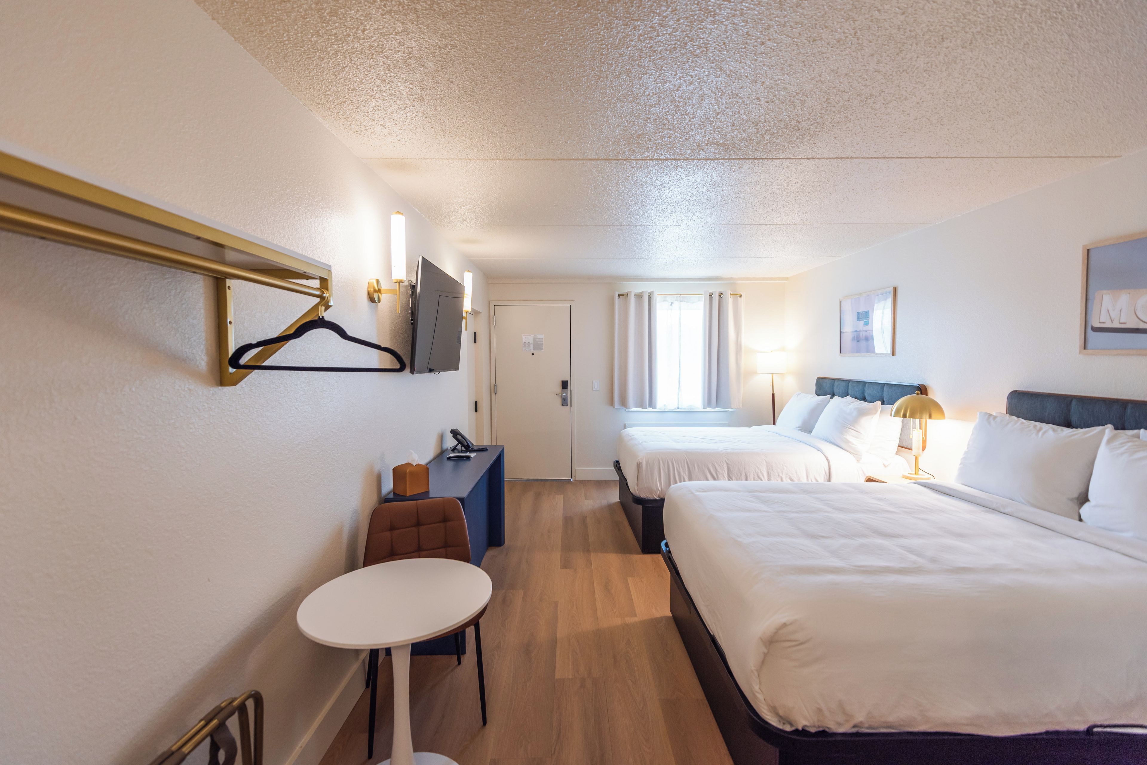Quarto de hotel com duas camas, uma escrivaninha, uma cadeira, uma televisão e uma janela com cortinas.