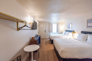 A hotel room with two beds, a desk, a chair, a television, and a window with curtains.
