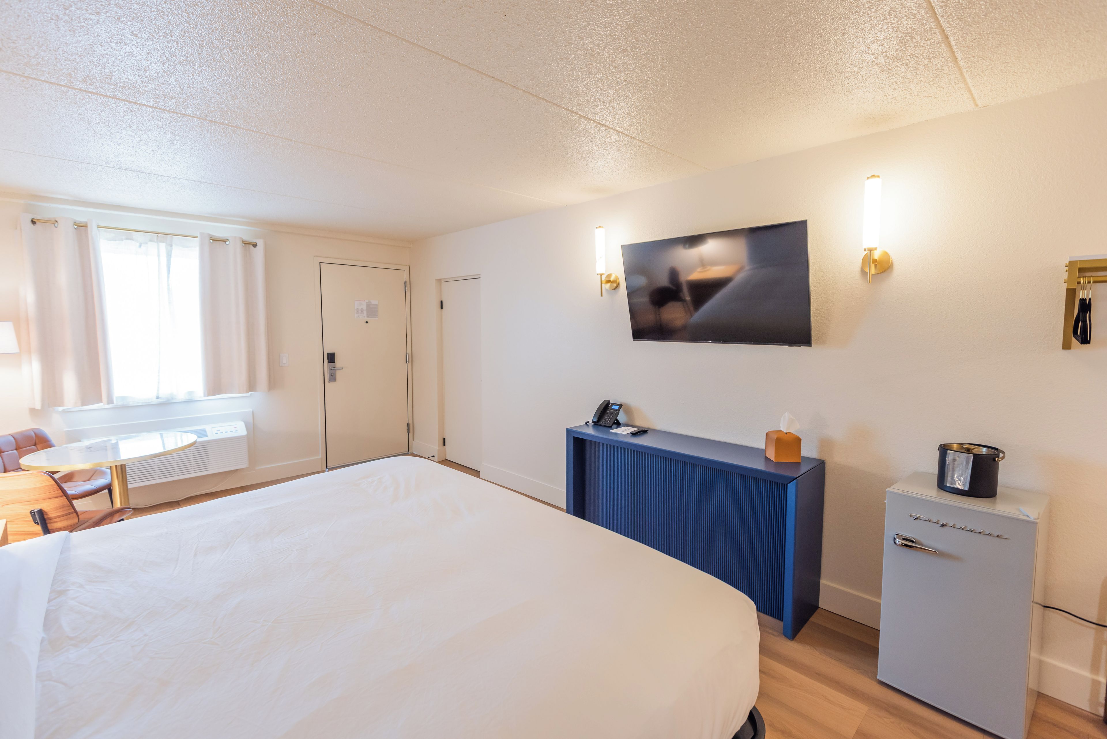 A hotel room with a large bed, a desk with a telephone, a small refrigerator, and a wall-mounted television.