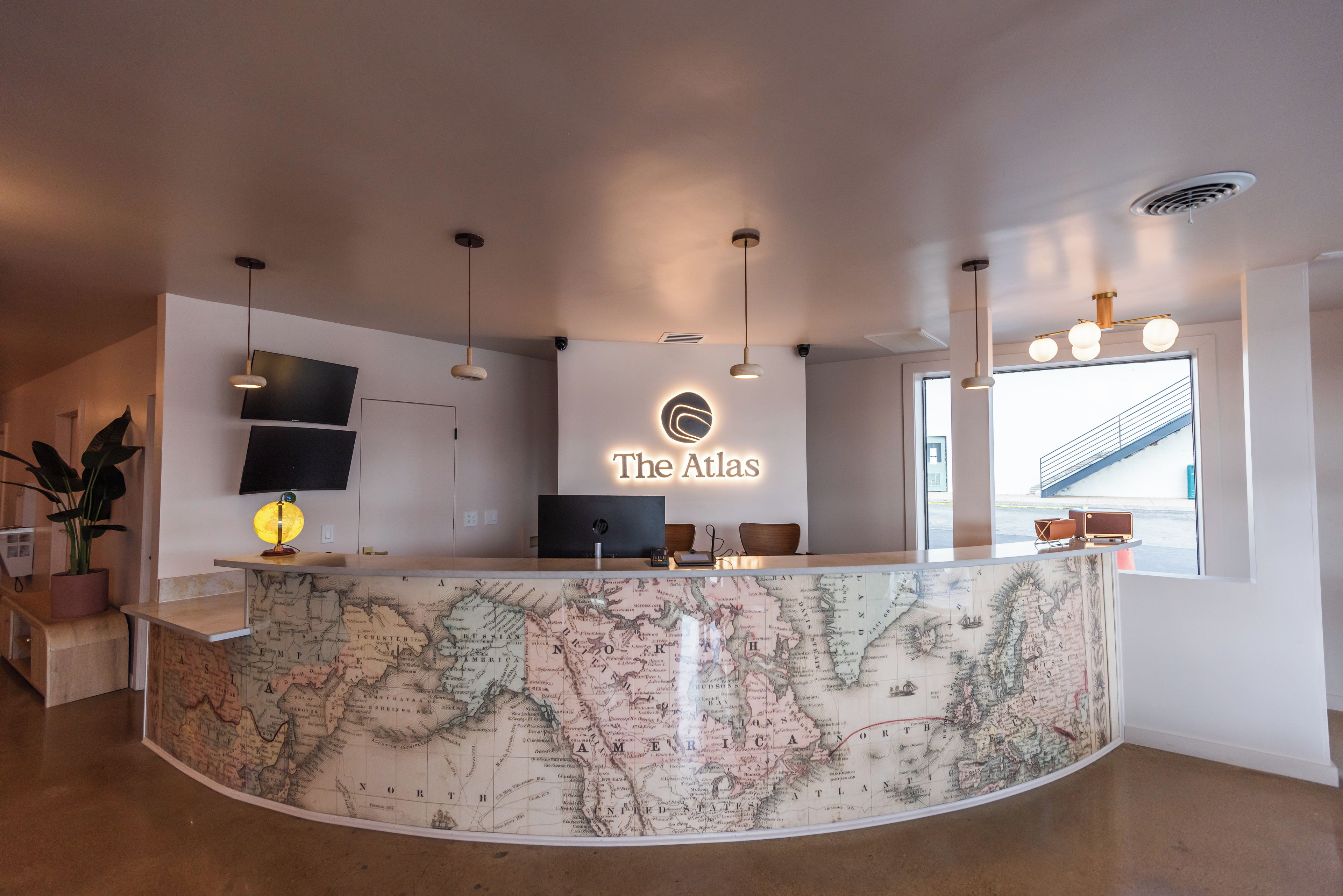 A reception desk with a map as a countertop, a flat-screen TV, and a sign that reads 'The Atlas'.