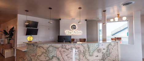 A reception desk with a map as a countertop, a flat-screen TV, and a sign that reads 'The Atlas'.