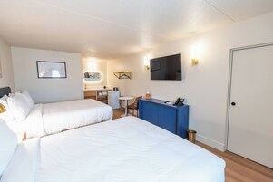 Habitación de hotel con dos camas, un escritorio, televisor y una puerta.