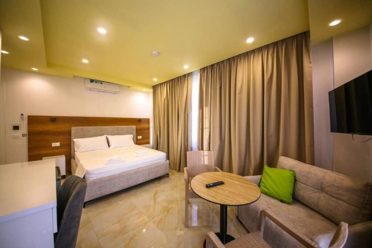 Une chambre d’hôtel avec un lit, une petite table ronde, un canapé et un téléviseur fixé au mur.