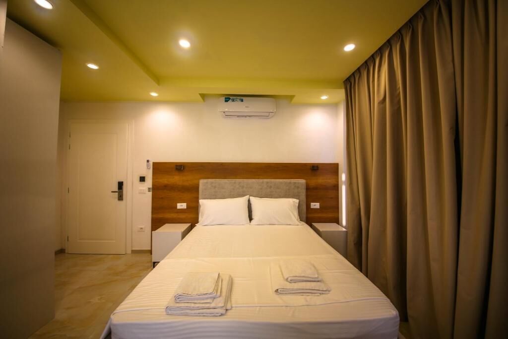 Een hotelkamer met een bed, nachtkastje, airconditioning en een deur.