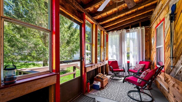 Eine Holzhütte mit Veranda, roten Stühlen, einer Bank und Blick auf den Wald.