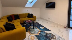 A modern living room with a yellow sofa, a patterned rug, a skylight, and a flat-screen TV. - SC Apartments (Bad Goisern am Hallstättersee)