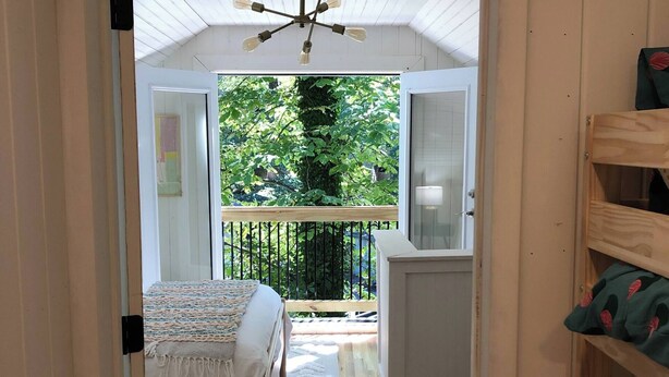 Ein Zimmer mit einem Bett, einem Fenster mit Blick auf Grünflächen, einer Deckenleuchte und einer Tür.
