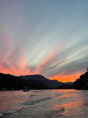 Een rivier met een boot, omgeven door bergen en een zonsondergang.