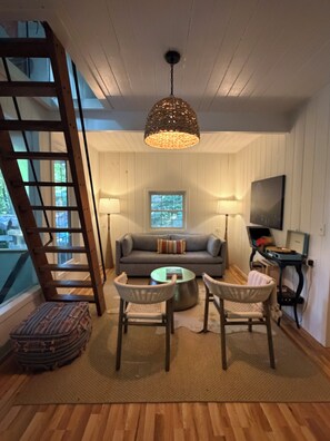 A room with a sofa, two chairs, a coffee table, a ladder, a television, and a window. - Lakefront Lake Lure Cabin: Private Dock, Paddleboards, Firepit Near Chimney Rock (Lake Lure)