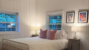 Ein Schlafzimmer mit einem Bett, zwei Nachttischen, einem Fenster und einem Deckenventilator.