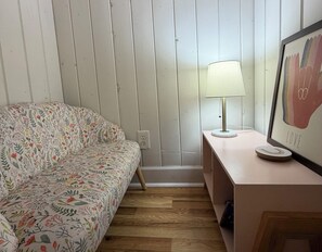 Une pièce avec un canapé à motifs, un lampadaire, un tableau encadré et un plancher en bois.