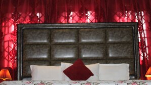 Quarto com uma cabeceira grande, colcha florida e cortinas vermelhas.