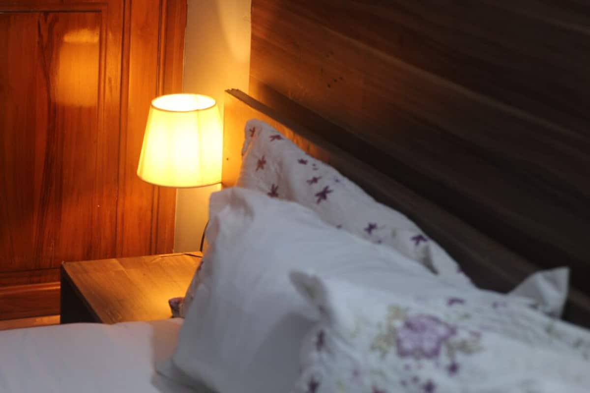 A bed with white bedding and a floral pattern, a wooden nightstand with a lamp, and a wooden headboard.