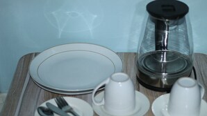 Uma mesa posta com pratos, copos e talheres, uma cafeteira e um recipiente de vidro.