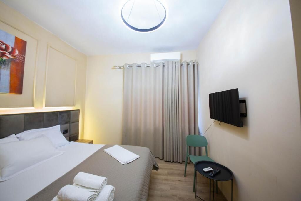 Una camera d'albergo con un letto, una sedia, una TV e una finestra con tende.