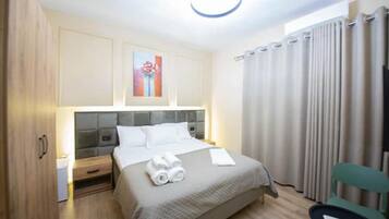 A hotel room with a bed, a nightstand, a chair, a TV, and a painting on the wall.