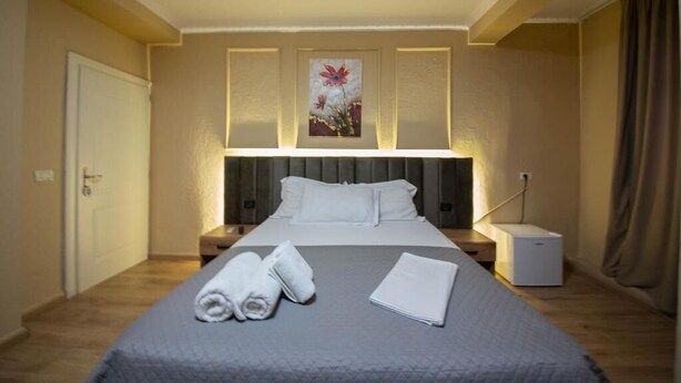 A hotel room with a bed, nightstands, a lamp, and a painting on the wall. - Eriks Rooms (Tirana)