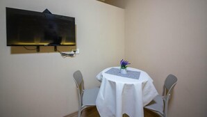 A dining area with a round table, two chairs, a wall-mounted TV, and a small vase with purple flowers. - Eriks Rooms (Tirana)