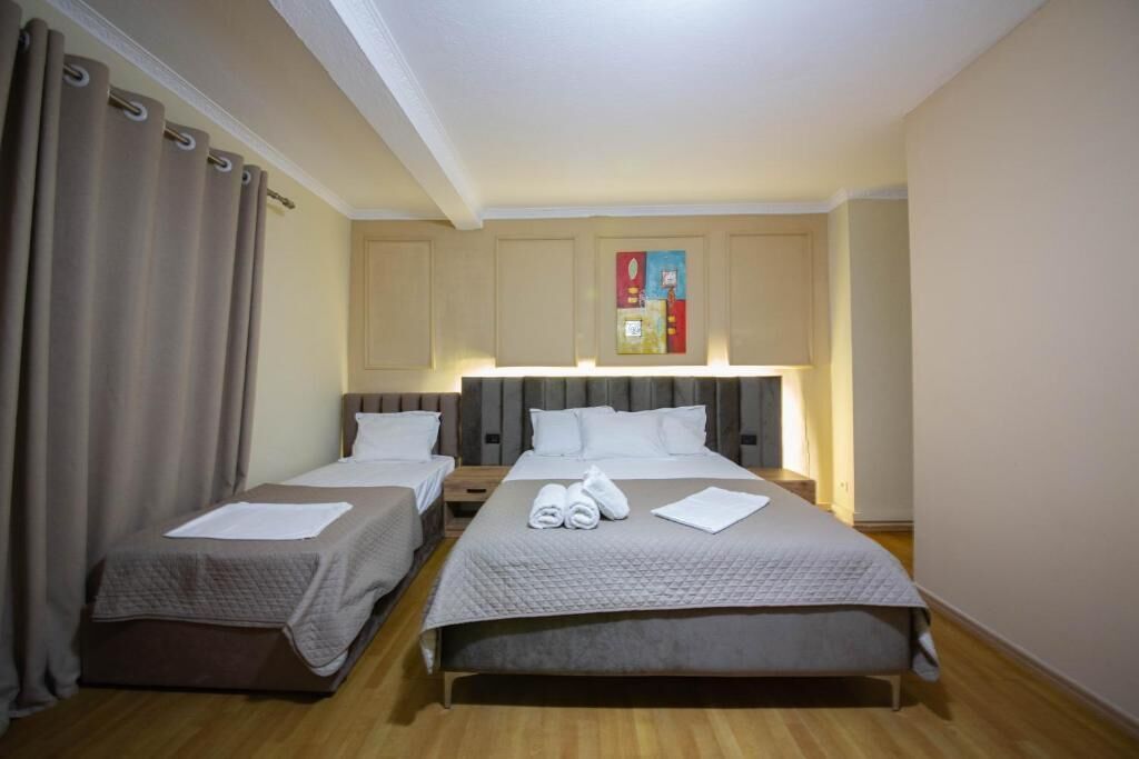 Ein Hotelzimmer mit zwei Einzelbetten, einem großen Bett, einem Nachttisch, einer Lampe und einem Gemälde an der Wand.