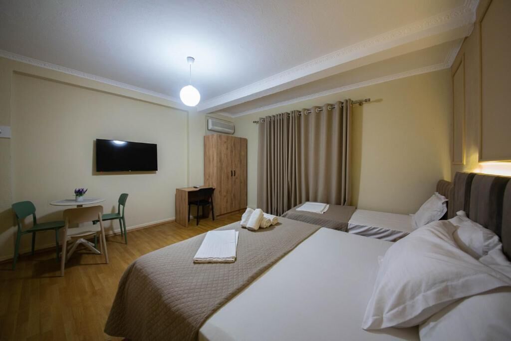 A hotel room with two beds, a desk, a chair, a television, and curtains.