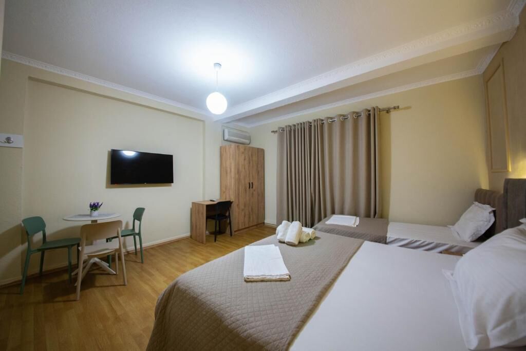 Ein Hotelzimmer mit Bett, Schreibtisch, Stuhl, Fernseher und einem fensterbepflanzten Fenster.