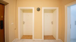 A hallway with two white doors, a clock on the wall, and a wooden floor. - Eriks Rooms (Tirana)