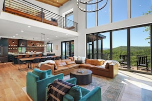 A spacious living area with a large sectional sofa, a coffee table, and a dining area with a kitchen in the background.