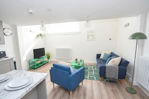 A modern living room with a blue sofa, a green coffee table, and a floor lamp. - Modern 1 Bedroom Central Leeds Mezzanine Apartment (Leeds)