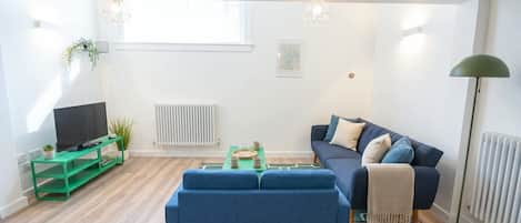 A modern living room with a blue sofa, a green coffee table, a television on a stand, and a floor lamp.
