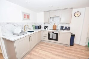 A modern kitchen with white cabinets, a marble backsplash, and a clock on the wall. - Modern 1 Bedroom Central Leeds Mezzanine Apartment (Leeds)