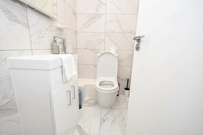A bathroom with a white sink, toilet, and marble tiles. - Modern 1 Bedroom Central Leeds Mezzanine Apartment (Leeds)