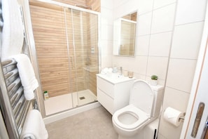 Ett badrum med en dusch som är avskärmad med glasväggar, en toalett, ett handfat med hygienartiklar och en liten krukväxt.