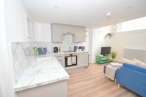 Eine moderne Küche mit Marmorarbeitsplatten, einem eingebauten Backofen und einem Essbereich mit einem blauen Sofa und einem kleinen Tisch.