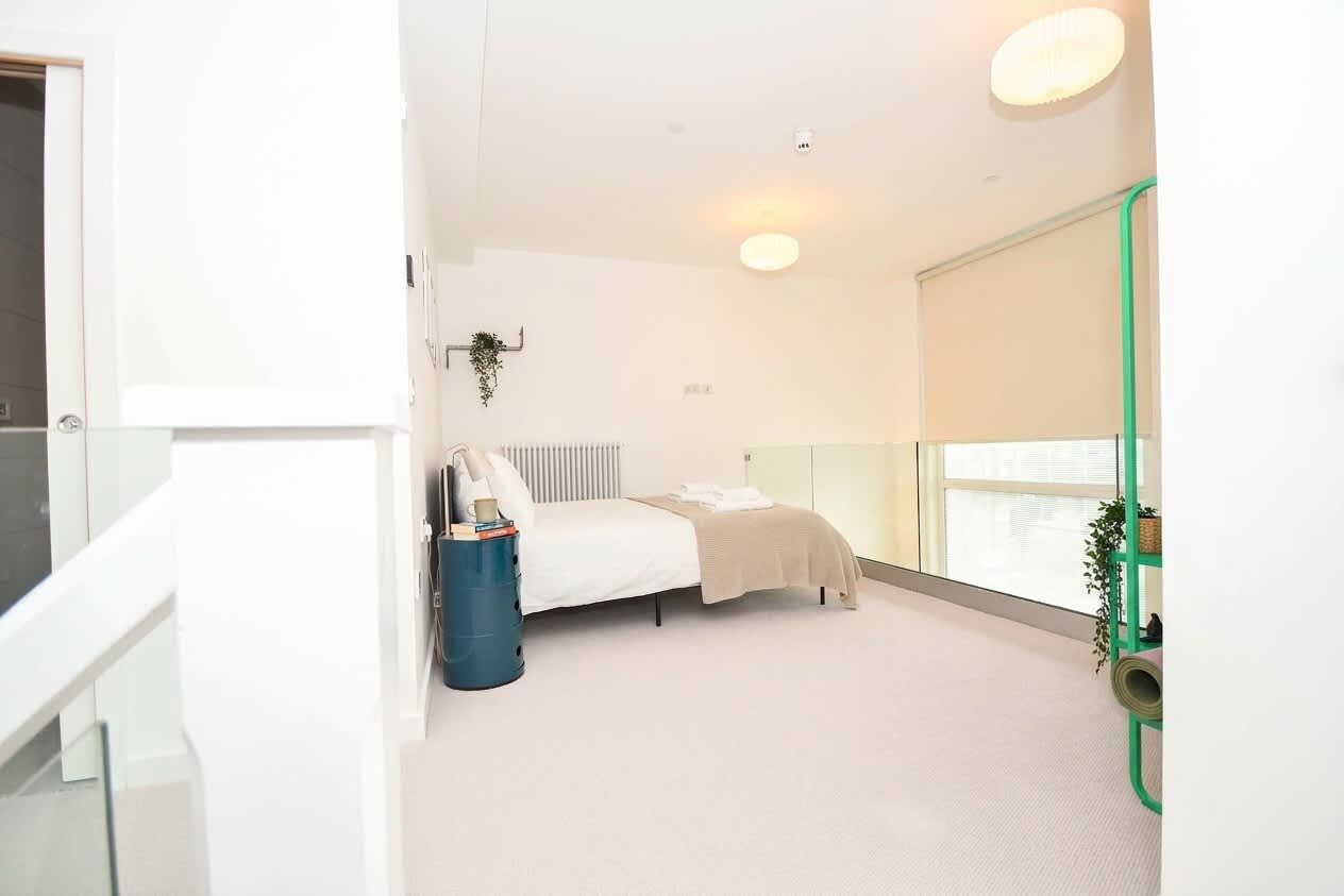 A bedroom with a bed, bedside table, radiator, window, and a green plant.