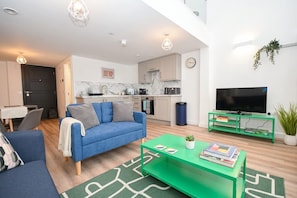 Ein modernes Wohnzimmer mit einem blauen Sofa, einem grünen Couchtisch und einem Flachbildfernseher.