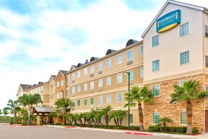 A Staybridge Suites hotel with a stone facade, multiple windows, and palm trees in front.