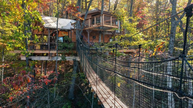 Una casa de madera con un balcón y un puente colgante en un bosque.