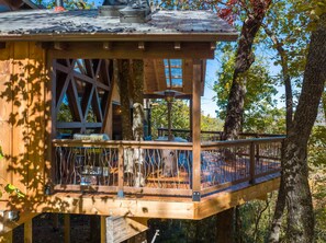 Eine Holzterrasse mit Geländer, Tisch und Stühlen, umgeben von Bäumen.