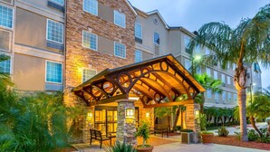 A hotel with a stone facade, outdoor seating area, and palm trees.