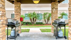 An outdoor patio with two gas grills, a gas tank, and a red fire extinguisher.