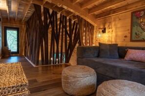 A wooden interior with a sofa, ottomans, and a decorative wall panel. - Nest-Shaped Cocoon Treehouse on 4 Trees - The Marsu (Highlands)