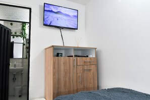 A bedroom with a bed, a wooden wardrobe, a television mounted on the wall, and a bathroom with a sink and mirror.
