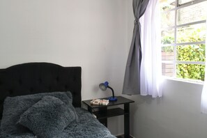 Une chambre à coucher avec un lit, une table de chevet avec une lampe et une fenêtre avec des rideaux.
