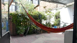 Un bâtiment en briques avec un hamac, des plantes en pot et des vélos.
