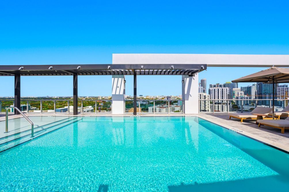 A rooftop pool with a city view, a pergola, and lounge chairs.