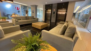A modern lobby with a sofa, chairs, a coffee table, and a potted plant. - Studio com vista Mar em Maceió - Max Rev (Maceió)