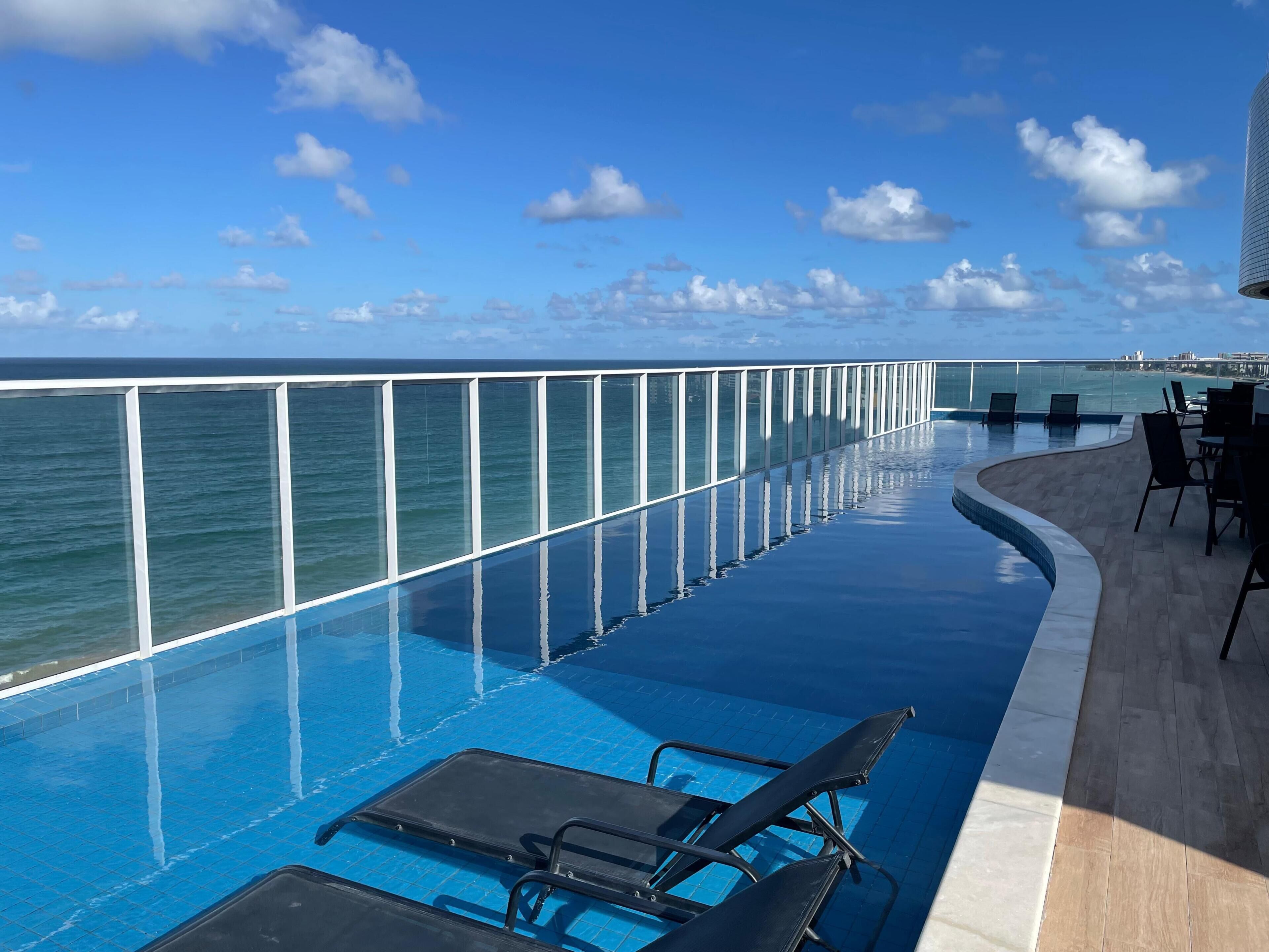 A poolside area with a glass railing, lounge chairs, and a view of the ocean.
