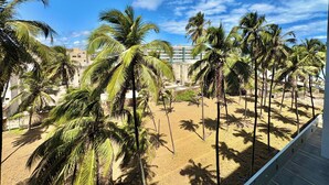 A sandy area with palm trees and a building in the background. - Studio com vista Mar em Maceió - Max Rev (Maceió)