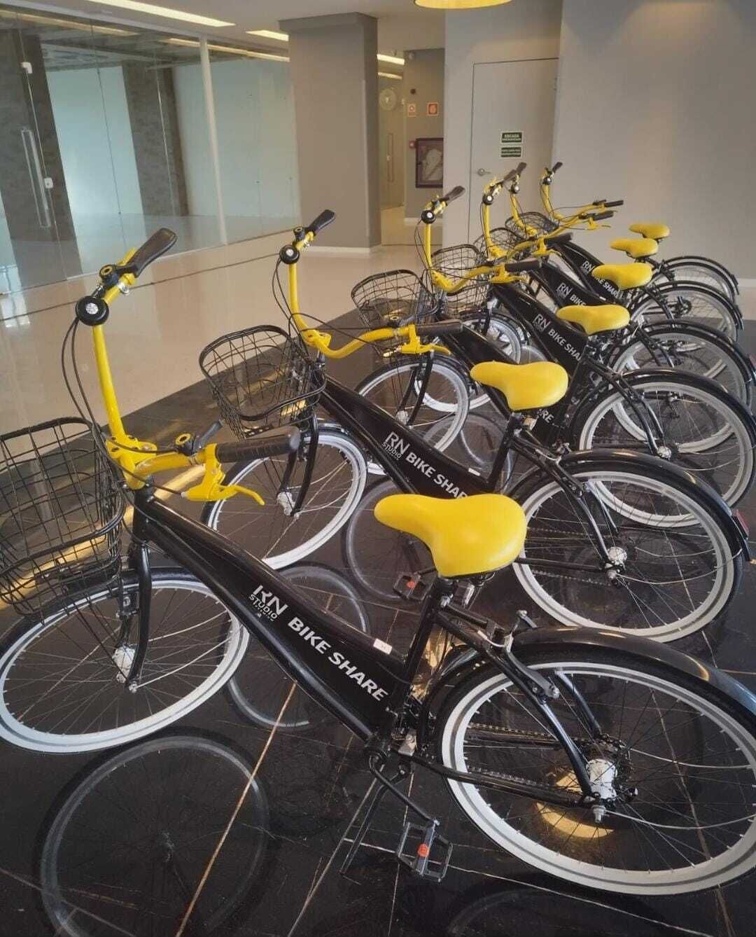 Eine Reihe von gelb-schwarz gestreiften Mietfahrrädern mit Körben, beschriftet mit „RN Bike Share“, in einer modernen Innenraumbedingung mit Glaswänden und einem sauberen, gefliesten Boden.