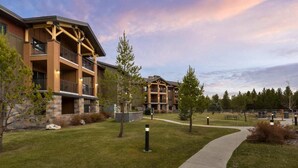 A multi-story building with balconies, a paved walkway, and a grassy area with trees. - Spacious 2-bedroom condo with Fireplace in majestic West Yellowstone (West Yellowstone)